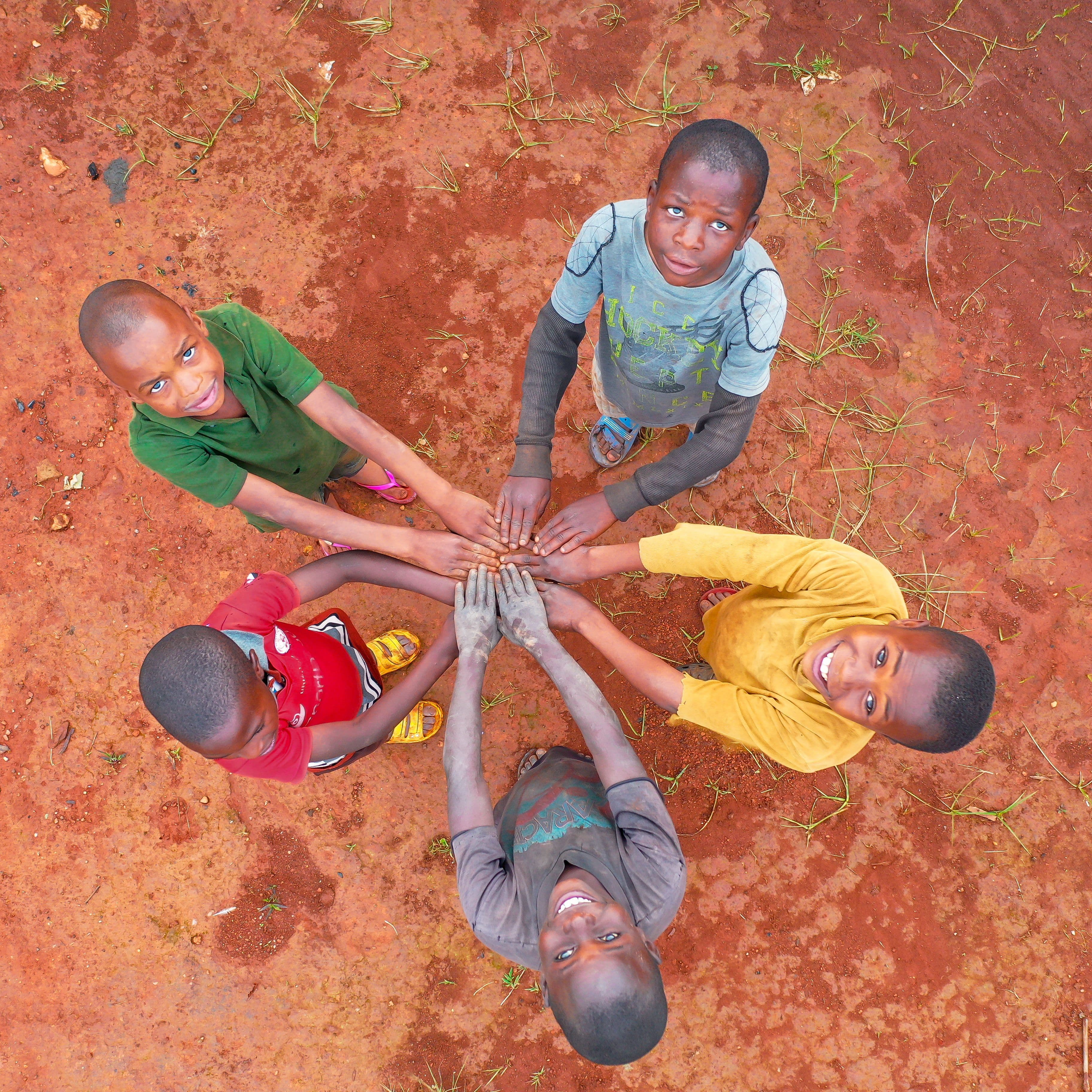 Kenyan children joining hands in a circle on warm earth, looking up together in unity and community